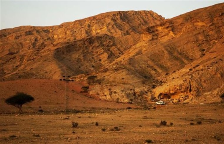 This undated handout photo provided by the journal Science shows a View of northern Jebel Faya from the north-east. The Jebel comprises Neogene limestones with rich seams of chert. The FAY-NE1 rockshelter is behind the white vehicle. Modern humans may have left Africa thousands of years earlier than previously thought, turning right and heading across the Red Sea into Arabia rather than down the Nile, an international team of researchers says. (AP Photo/Science)